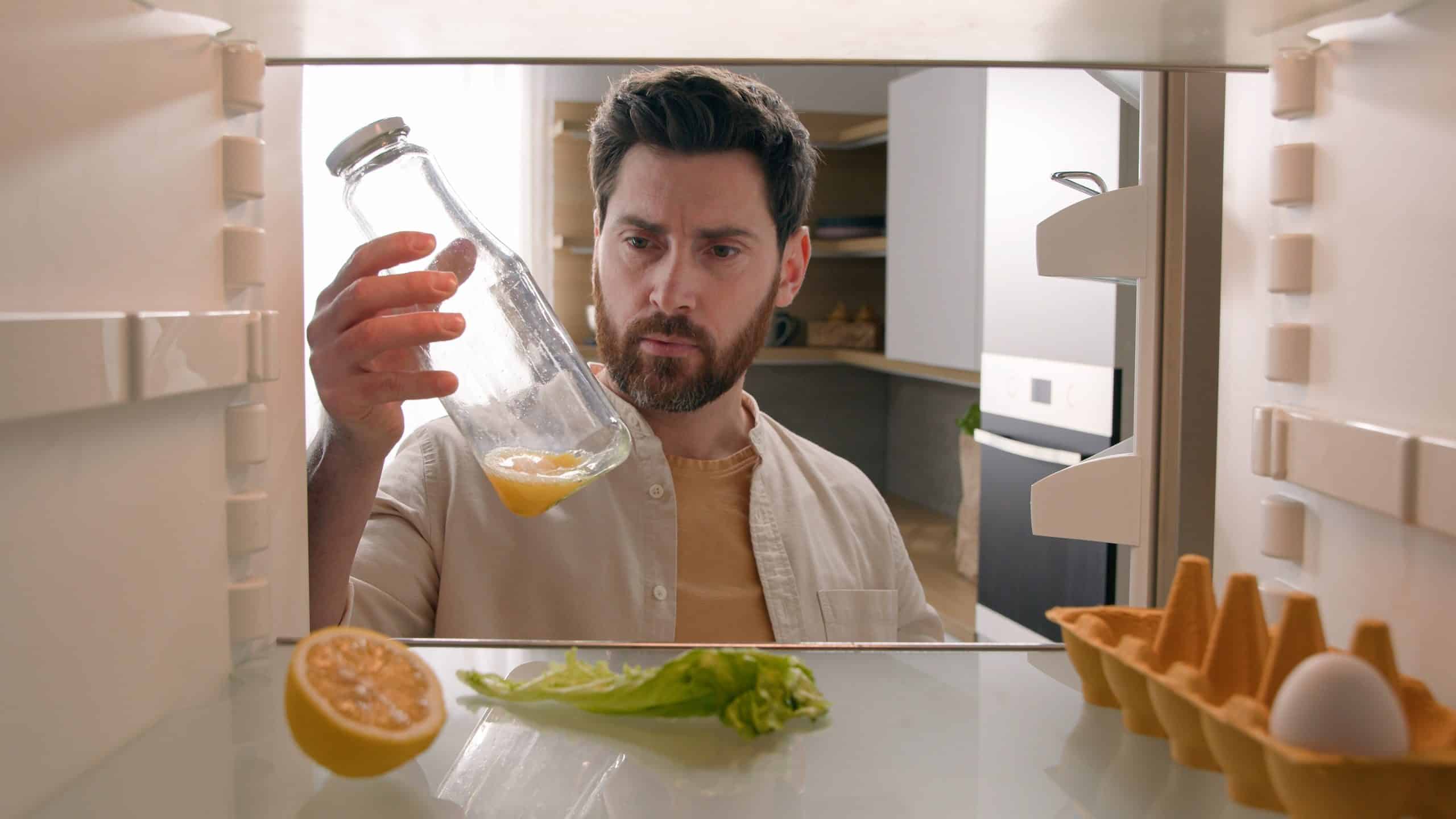 Man open empty refrigerator with half lemon lettuce leaf one egg slice of bread leftover orange juice in bottle find solution order food delivery with mobile phone app point of view from inside fridge