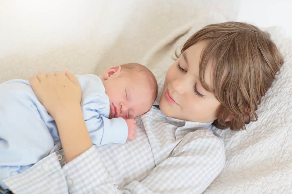 Siblings meet newborn baby. Child holding new infant brother for the first time. Kids visit mother in labor and delivery ward after birth of new baby. Sibling love. Family bonding.