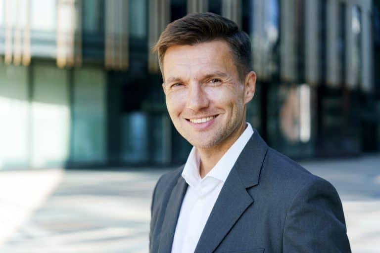 Confident businessman in a suit smiles at the camera outside a modern office building
