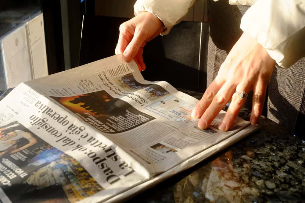 Lombardy, Italy March 1st 2025 Woman's hands holding Italian newspaper La Stretta, resting on marble surface bathed in soft sunlight