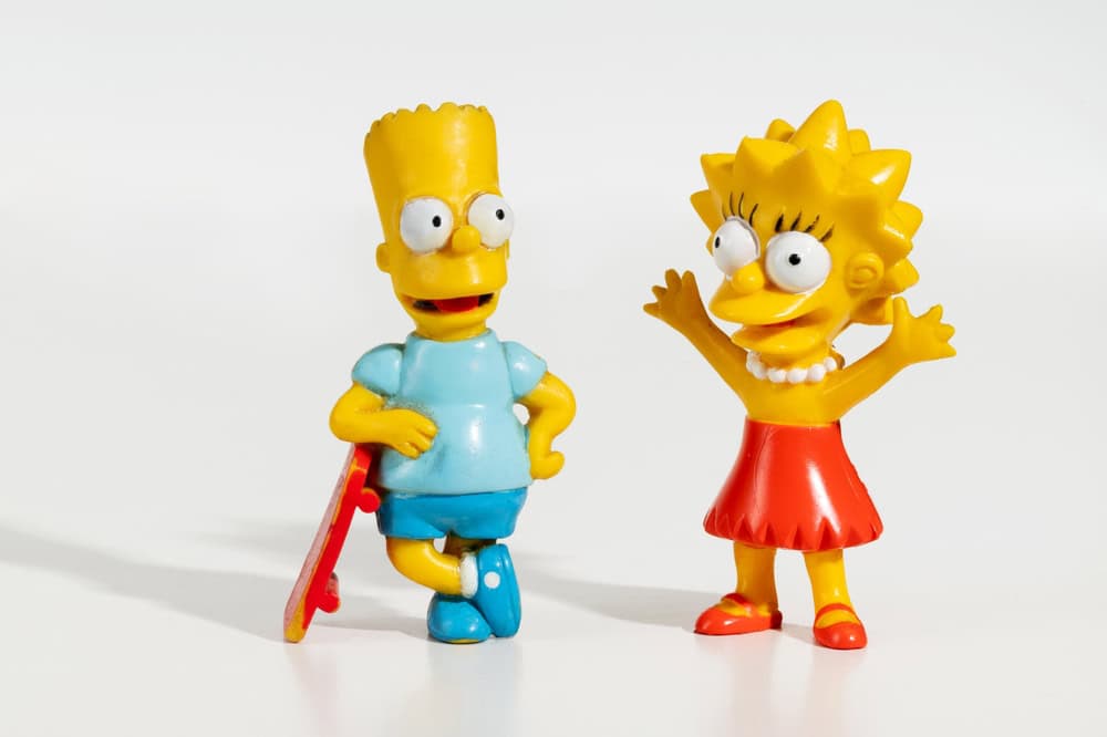 Milan, Lombardy, Italy - February 6, 2025: Bart Simpson leaning on skateboard and Lisa Simpson with arms raised, two figurines on white background