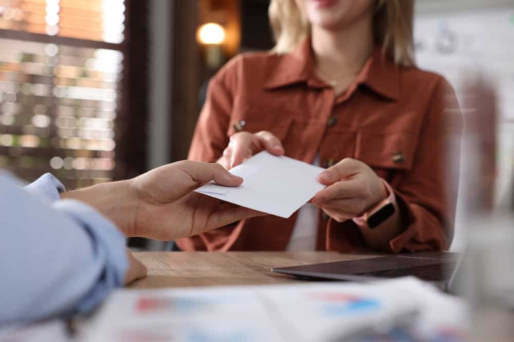Money bonus. Employee receiving envelope from boss in office, closeup