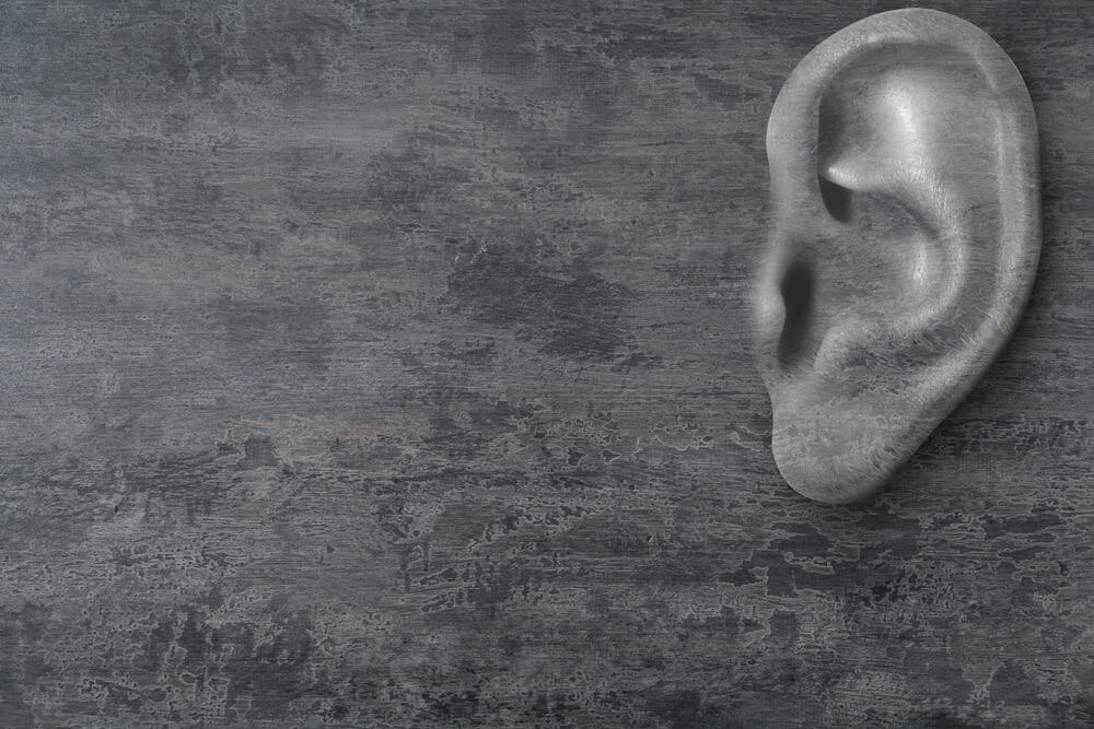 Human ear in grey stone wall, space for text. Eavesdropping, concept that even walls have ears
