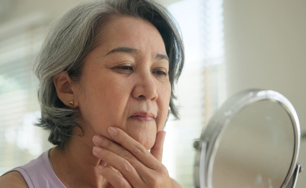 Asia adult people middle age old woman look at mirror dry skin face hand touch neck cheek stress sad at home elder health care aging beauty issue. Asian female aged eye botox filler plastic surgery.