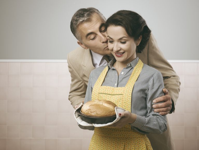 Vintage husband kissing her wife, she is holding a delicious home made cake