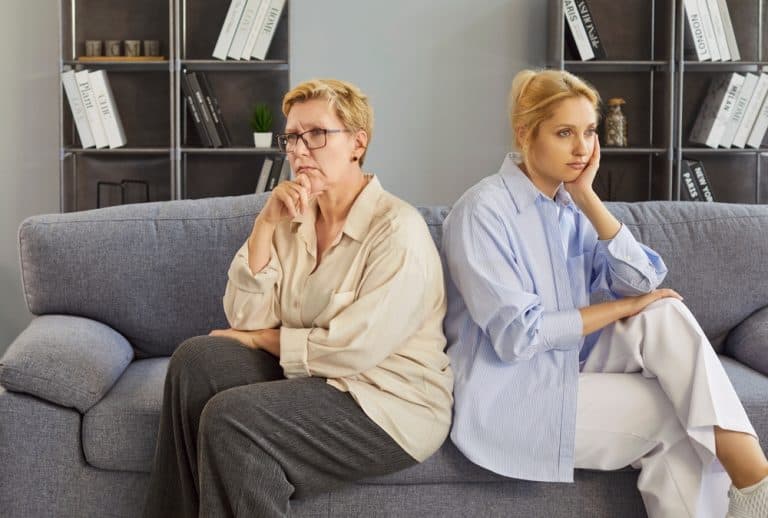 Mother and daughter home conflict, sitting back-to-back on sofa, senior adult and young woman upset in disagreement, tension, misunderstanding between close family members or female friends