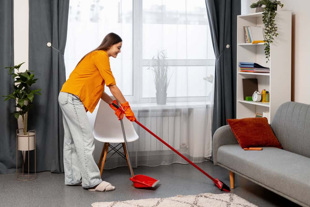 Young woman sweeping the floor, maintaining a tidy home and completing domestic housework