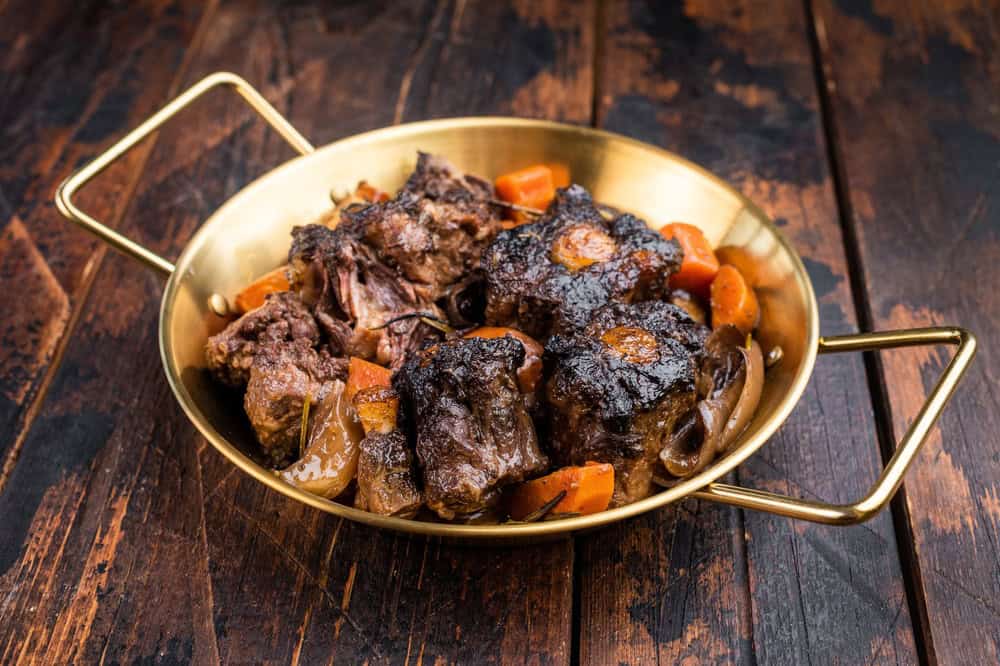 Homemade beef oxtail ragout in pan, gelatin rich slow cooked meat with vegetables in dark sauce, overhead shot.
