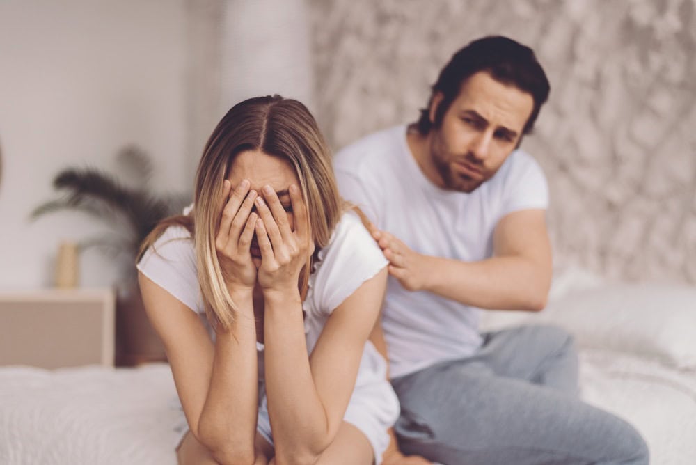 Couple Sitting on Bed With Woman Covering Her Face and Man Showing Concern in a Quiet Room