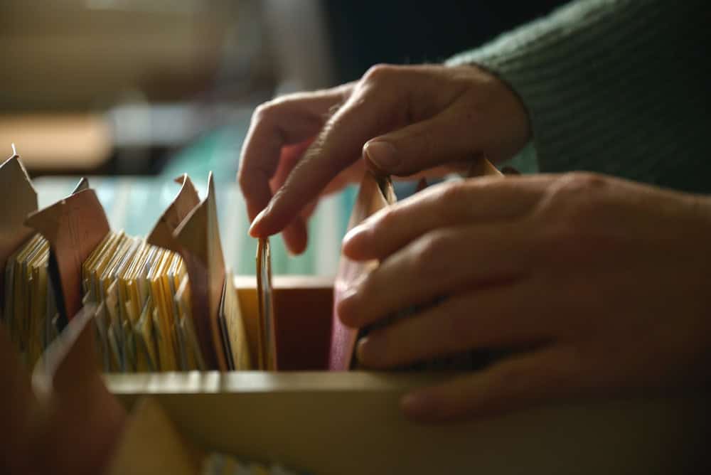 Close-up of female hands browsing old card catalog drawers, vintage library research concept, selective focus