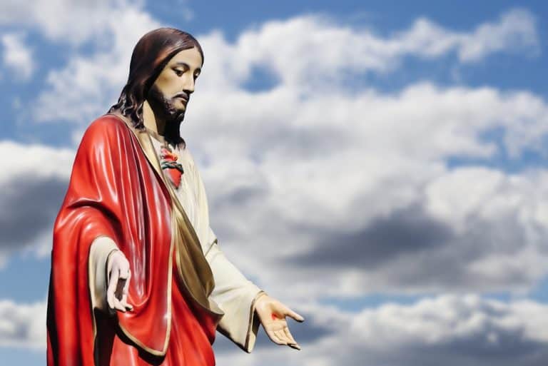 Sacred Heart of Jesus statue against cloudy blue sky. Christian religious symbol outdoors with copy space. Faith spirituality prayer worship and Catholic devotion concept for believers.
