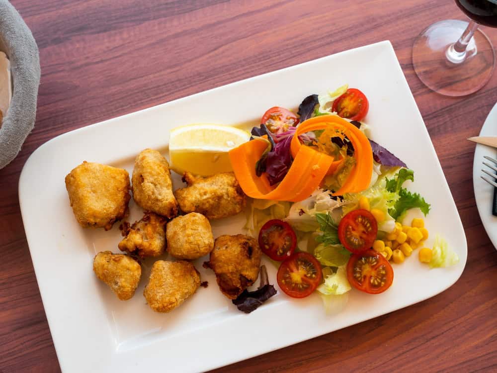 Pickled dogfish with chopped carrot, basil, lettuce and cherry tomatoes served on white flat plate.