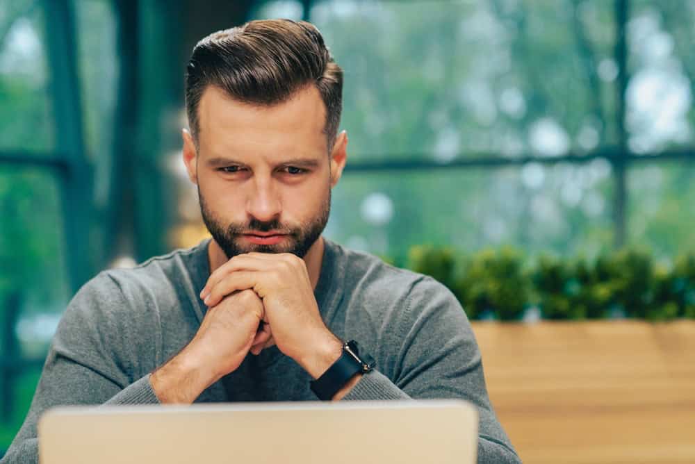 Serious man focusing on laptop screen in modern office space, deep in thought while working remotely in a stylish coworking cafe, professional businessman concept