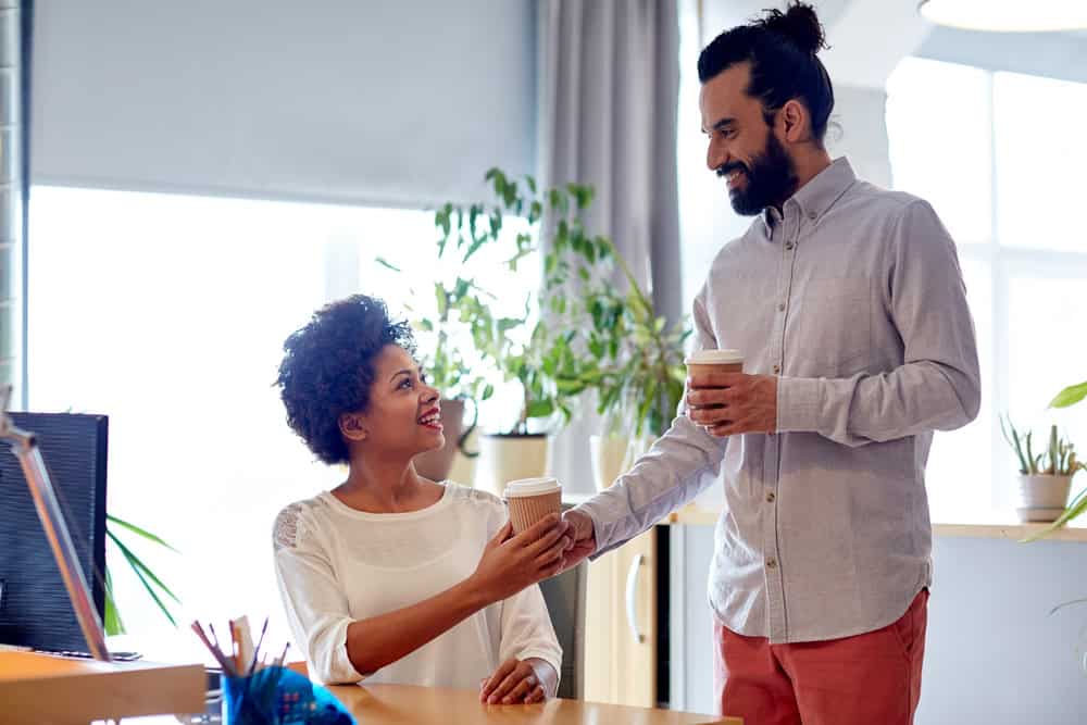 Happy man bringing coffee to woman in office