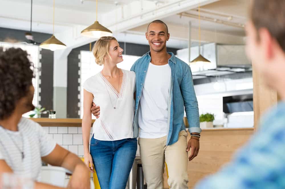 Happy cheerful african man introducing his beautiful girlfriend to his friends. Happy friends meeting over weekend to enjoy. Happy guys waiting their couple friend at coffee shop.