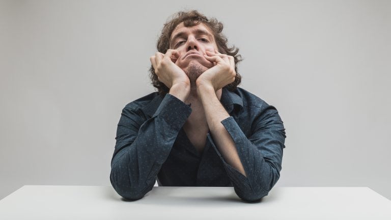 portrait of young bored man thinking with his face deformed on a gray background