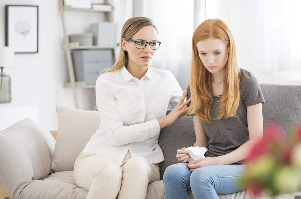 Mother in glasses comforting unhappy teenage daughter holding white handkerchief