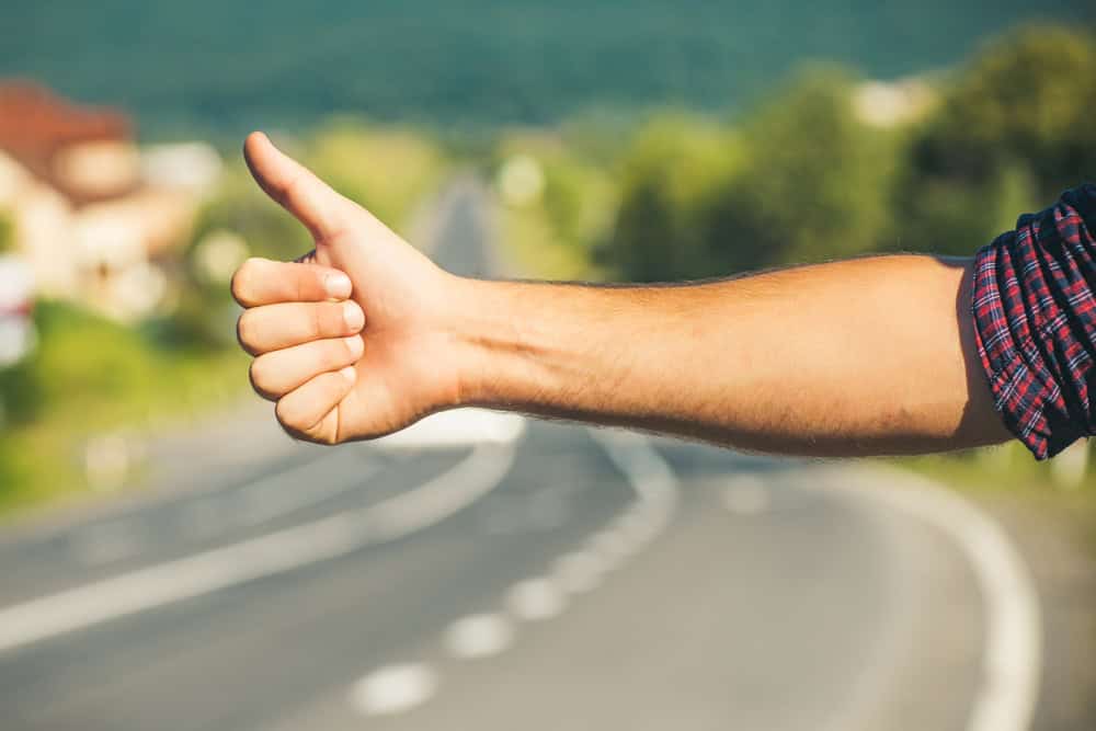 Travel, trip, vacation, wanderlust. Hitchhiker sign on road. Thumbs up male hand gesture outdoors. Hitchhiking, hitching, thumbing, auto stop concept.