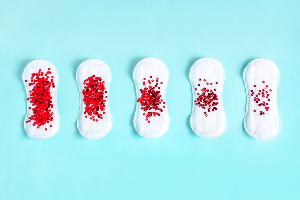Menstrual pad with red glitter on blue colored background. Minimalist still life photography concept
