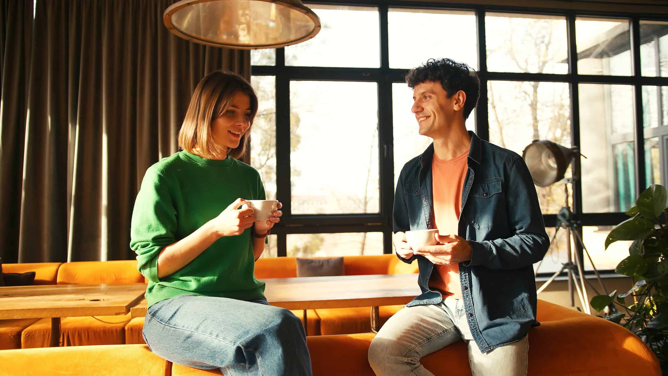 Cheerful young man and woman enjoying lively conversation while drinking coffee in modern, sunlit cafe, creating warm and relaxed atmosphere coffee. Break concept