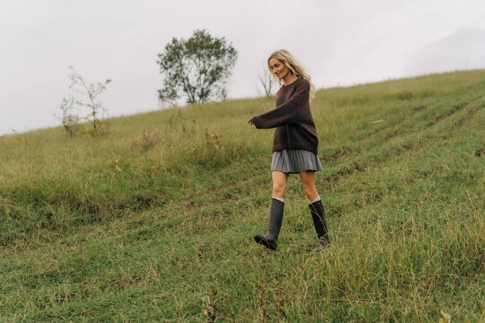 A beautiful happy cheerful woman in high rubber boots walks through an autumn field.