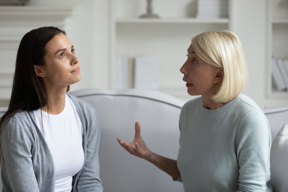 Strict anxious mature mother lecturing scolding annoyed grown daughter, sitting on sofa at home, parent and child quarrel, generations conflict, stubborn young woman ignoring angry senior mum