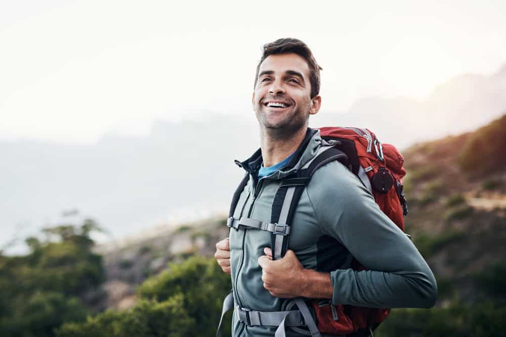 Man, backpack and thinking in outdoor forest for wilderness experience, exploration and solitude for stress relief or mental health. Guy, nature and hiking in woods for adventure or physical exercise