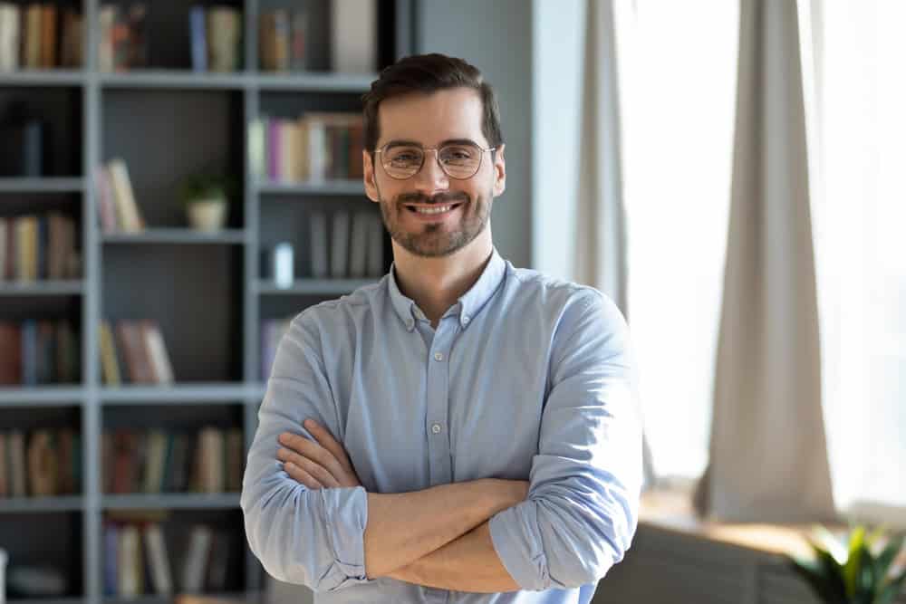 Happy and confident. Proud smiling young man entrepreneur manager teacher pose for portrait in modern office library looking at camera enjoy successful career profitable business personal achievement