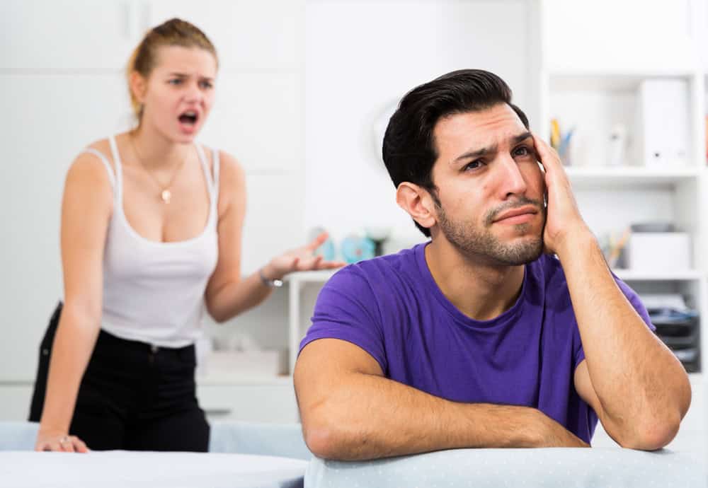 Young stressed man at home table with screaming wife behind