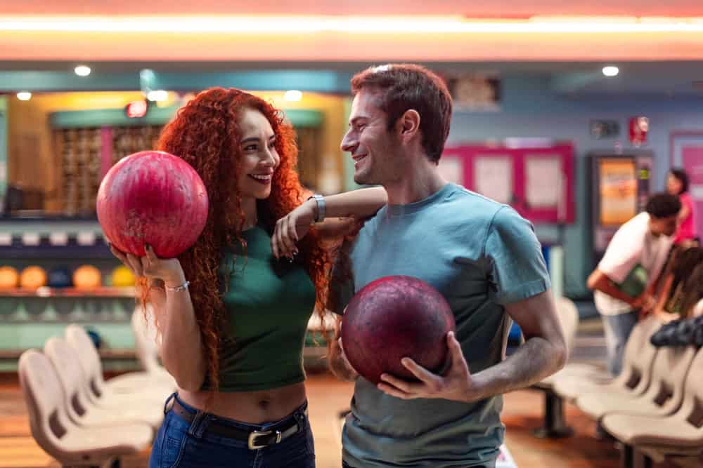 Young couple holding bowling balls, smiling joyfully at each other while enjoying a fun day at the bowling alley together
