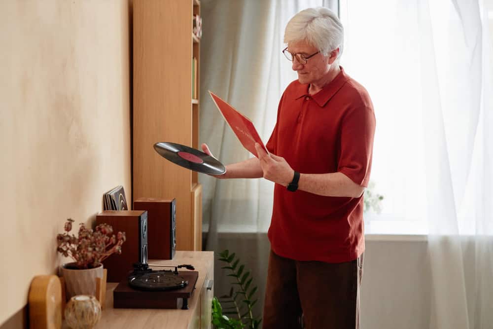 Side view portrait of white haired senior man holding vinyl records and choosing quiet home entertainment for relaxing evening copy space