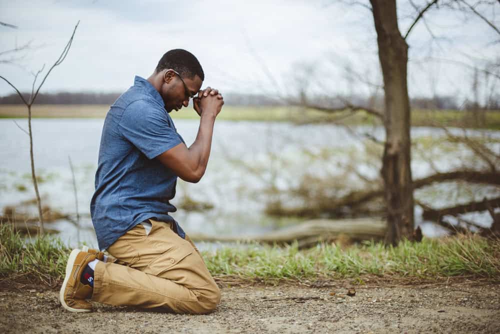 A vertical shot of an African-American male praying on his knees