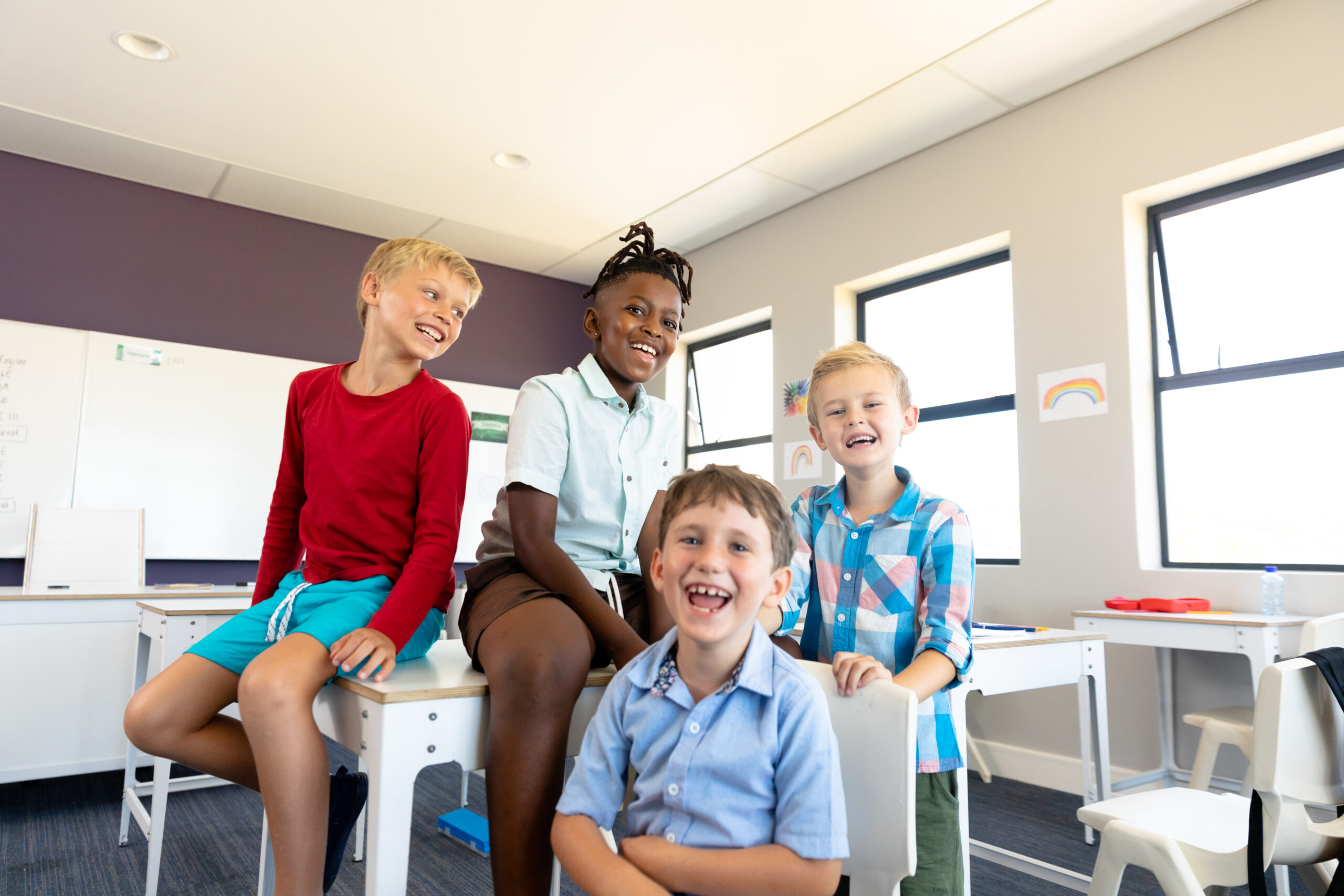 Portrait of cheerful multiracial elementary schoolboys sitting at desk in classroom. unaltered, childhood, together, enjoyment, education and back to school concept.