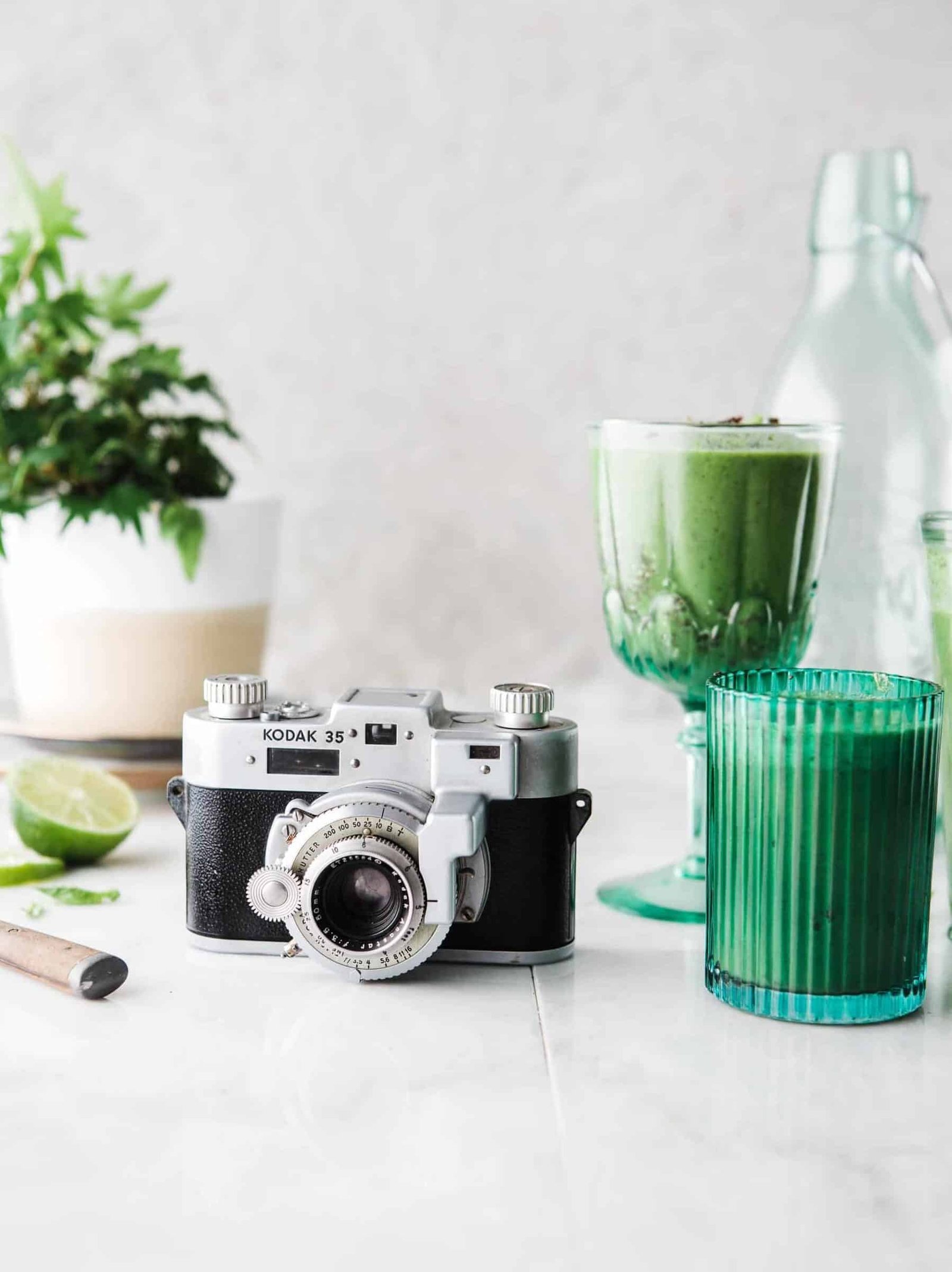 Vintage camera with green smoothie and glasses on a white table, styled for lifestyle photography.
