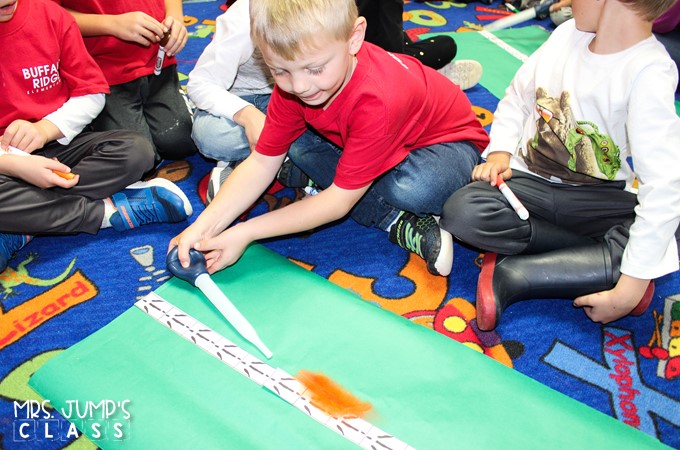 A young boy uses a baster to blow an orange feather down a measurement chart
