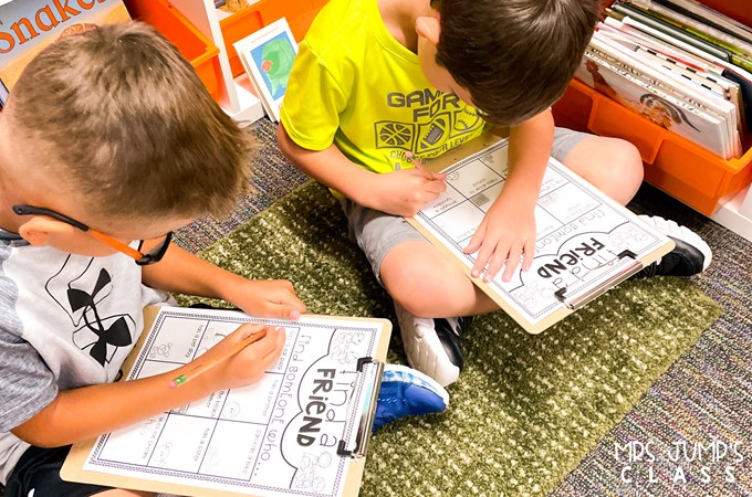 Two boys sit on a carpet with clipboards, completing a "Find a Friend" worksheet