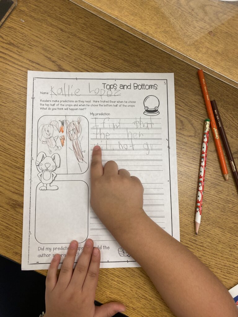 A student pointing at their writing on a prediction worksheet