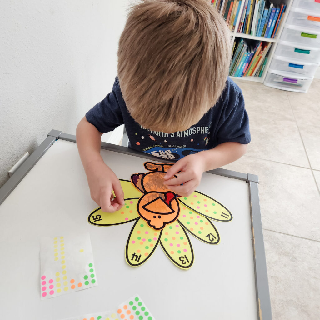 A young child adds dot stickers to feathers on a paper turkey