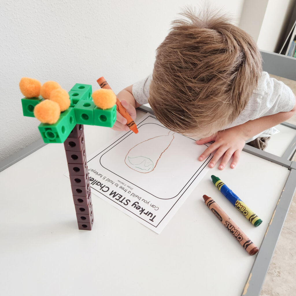 A child writes on a worksheet with a snap cube tree next to him.