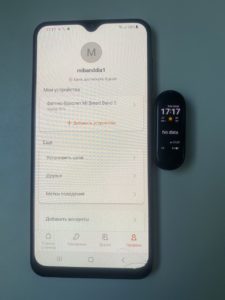 Мобільний телефон з відкритим додатком для моніторингу здоров'я та фітнесу, поруч фітнес-браслет на чорному фоні.
