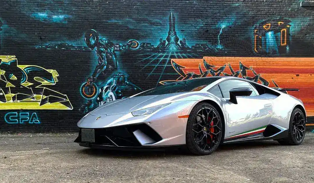 Silver Lamborghini Huracan sports car in front of colorful graffiti wall.