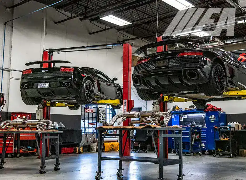 Two black sports cars on lifts in a professional auto repair shop.