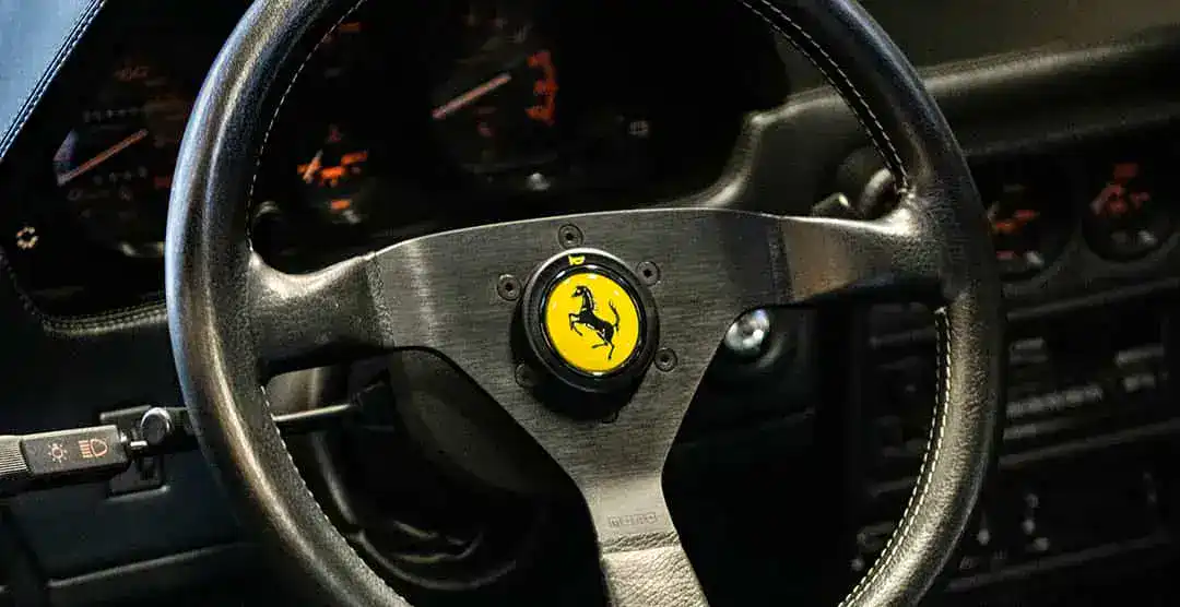Close-up of Ferrari 328 GTS steering wheel with prancing horse emblem.