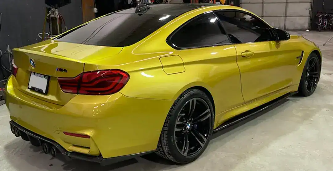 Yellow BMW M4 coupe with black wheels in a garage setting.