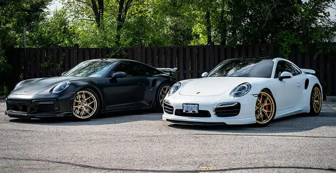 Black and white Porsche sports cars parked outdoors with trees in background.