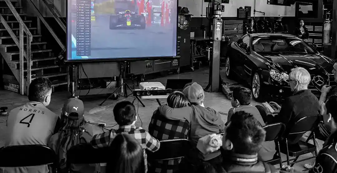 People watching F1 race on large screen at Miami automotive event.