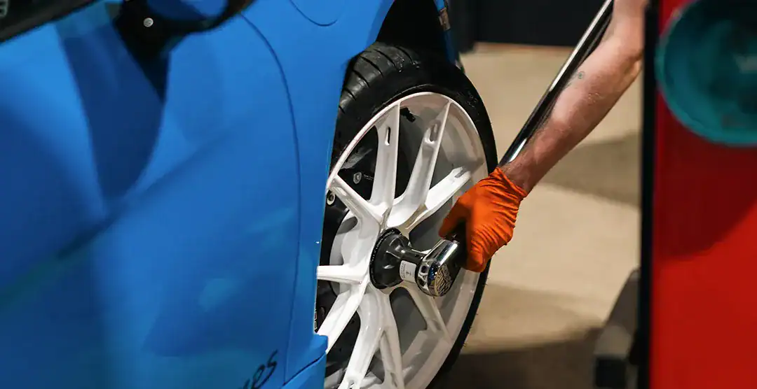 Technician changing a car tire on a blue sports car at a service center.