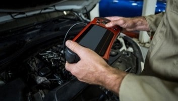 Diagnostic scanner being used by auto technician under the hood of a vehicle.