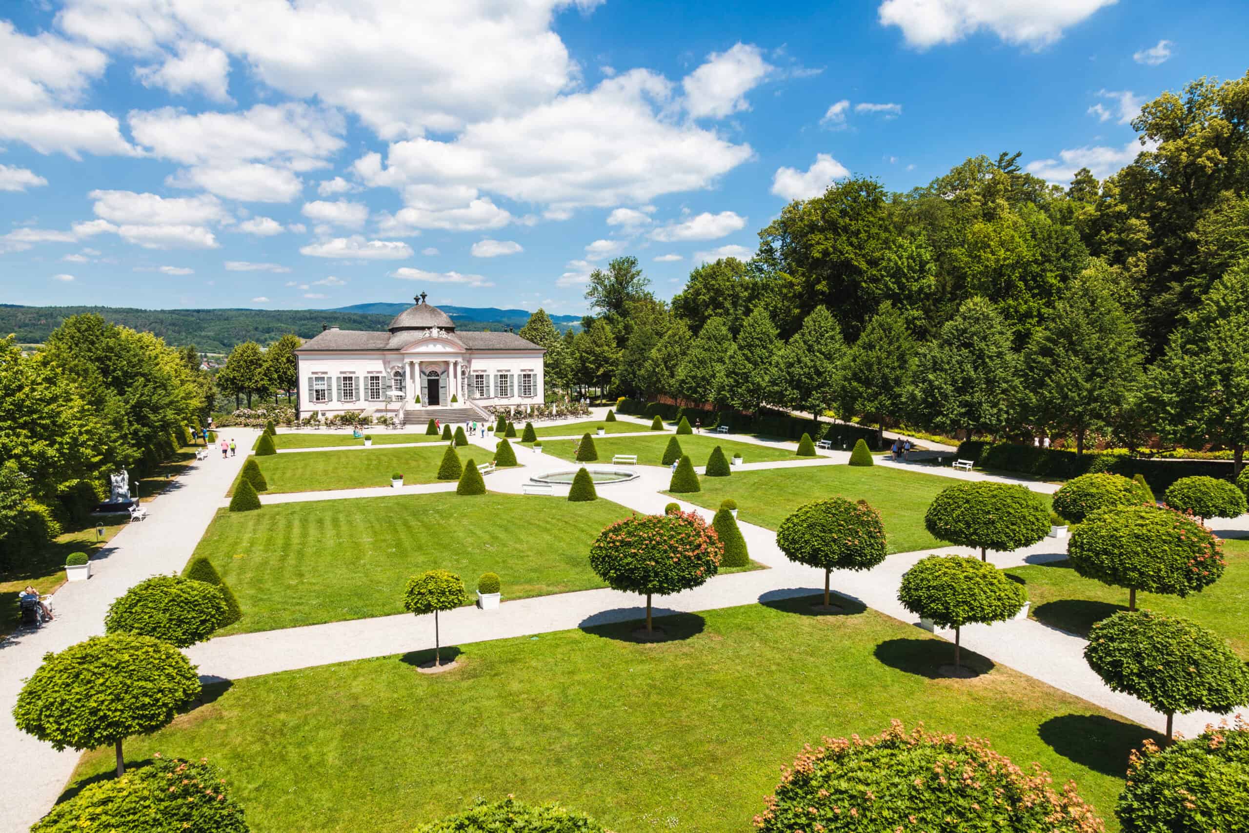 Elegant mansion with manicured gardens and lush greenery in a scenic landscape.