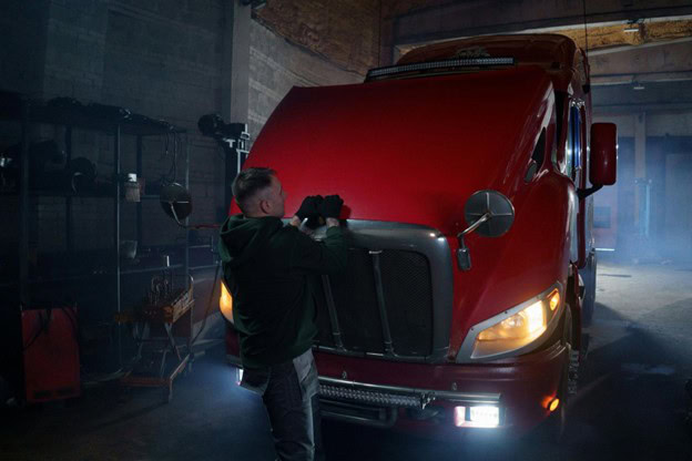 Technician inspecting a red semi-truck engine in a garage setting.